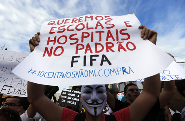 A demonstrator wearing a Guy Fawkes mask holds up a sign during a protest against the Confederations Cup and President Dilma Rousseff's government, in Recife City June 20, 2013. Brazil's biggest protests in two decades intensified on Thursday despite government concessions meant to quell the demonstrations. The sign reads "We want schools and hospitals, not FIFA standards". REUTERS/Marcos Brindicci (BRAZIL - Tags: CIVIL UNREST POLITICS SPORT SOCCER)